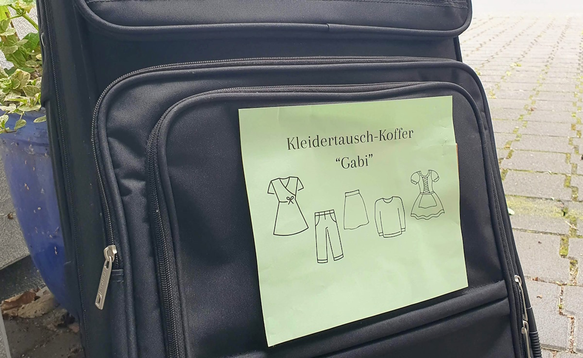 Koffer mit grünem Zettel, auf dem steht, Kleidertausch-Koffer.
