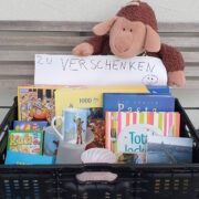 Kiste mit Büchern, Spielen, einem Kuscheltier und dem Schild "Zu verschenken".