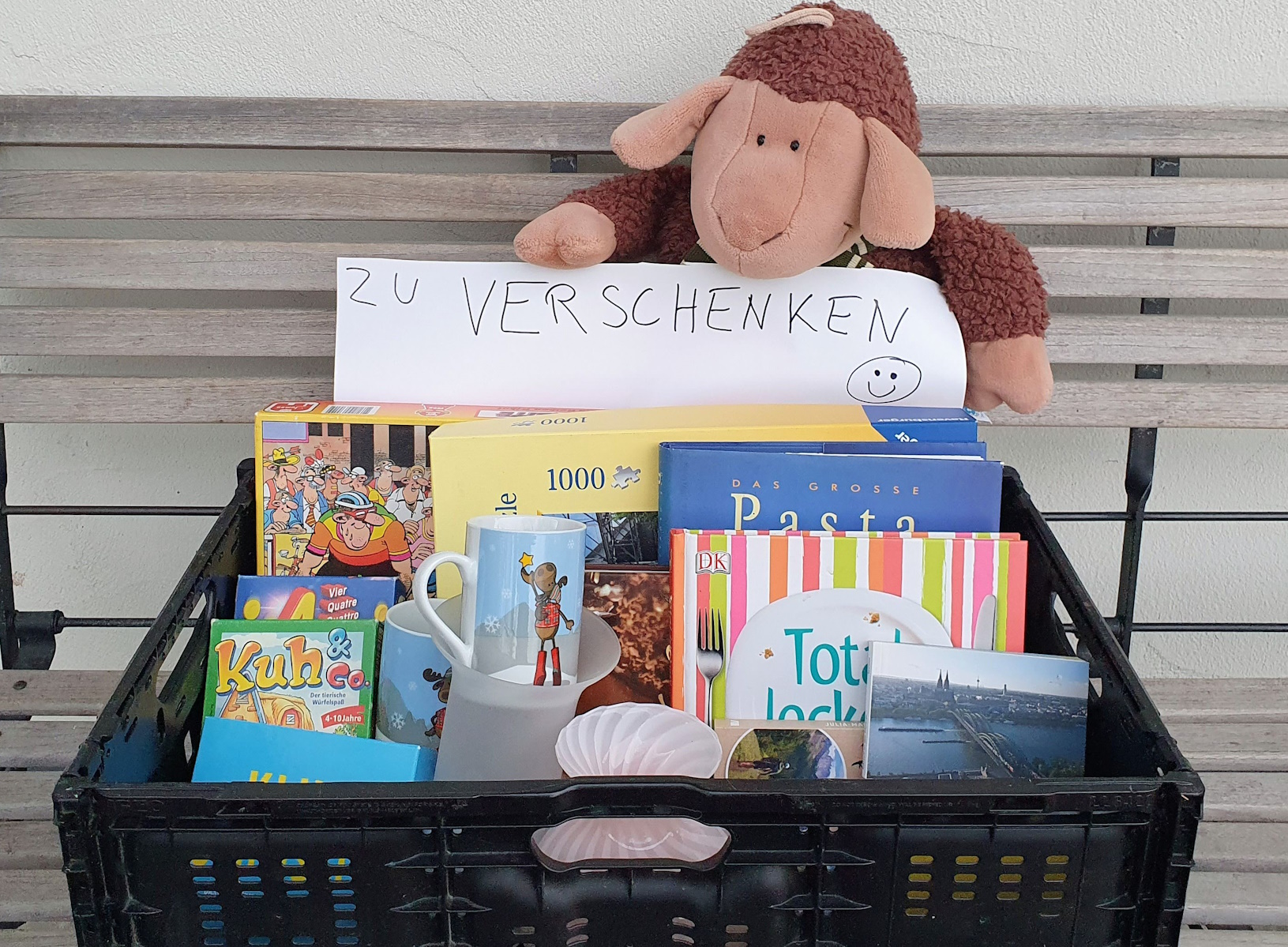Kiste mit Büchern, Spielen, einem Kuscheltier und dem Schild "Zu verschenken".