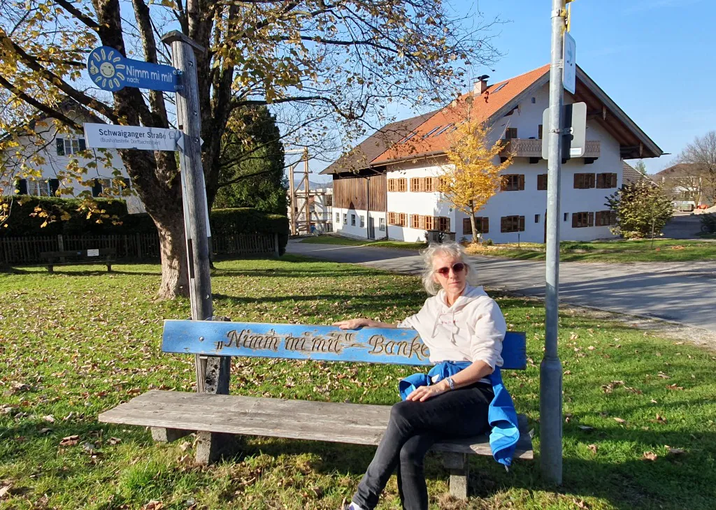 Mitfahrerbank im ländlichen Raum, auf der eine Frau sitzt