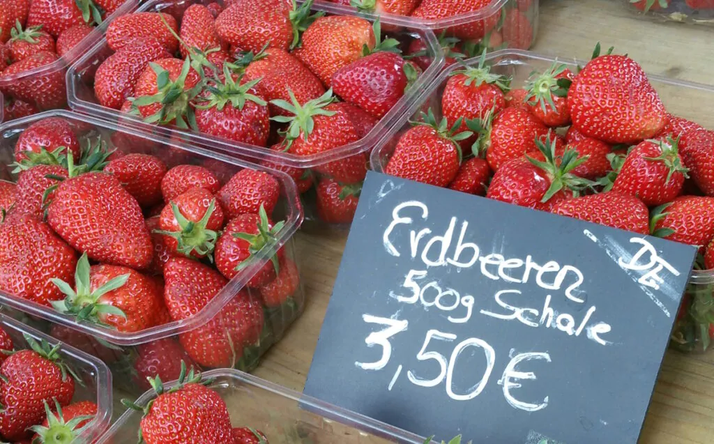 Erdbeeren_Markt Erdbeeren in Plastikschalen mit einem Schild auf dem steht: DE - Erdbeeren 500 g Schale 3,50 Euro.