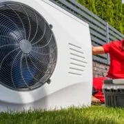 Ein Installateur kniet neben einer Wärmepumpe.