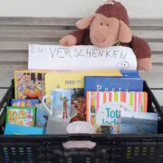 Kiste mit Büchern, Spielen, einem Kuscheltier und dem Schild "Zu verschenken".
