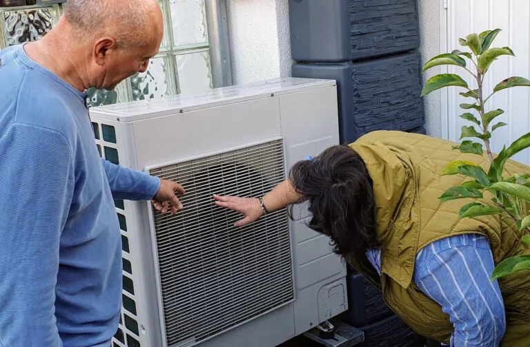 Eine Mann und eine Frau stehen neben einer Waermepumpe.